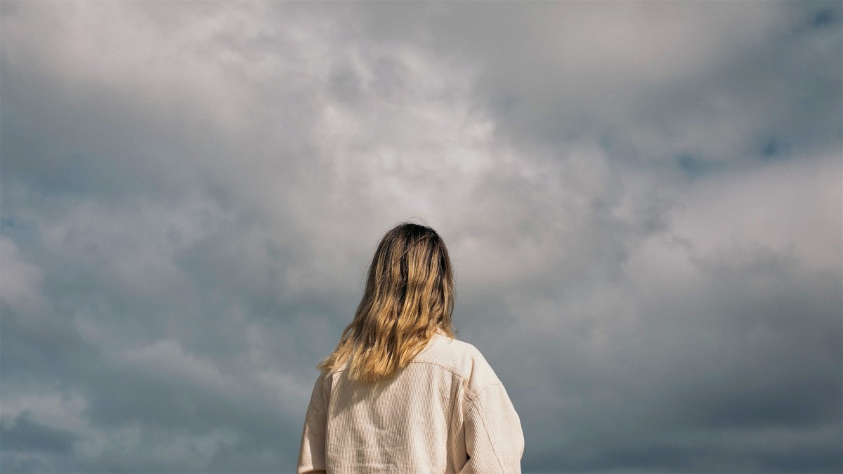 A blonde woman is backdropped by a cloudy gray sky
